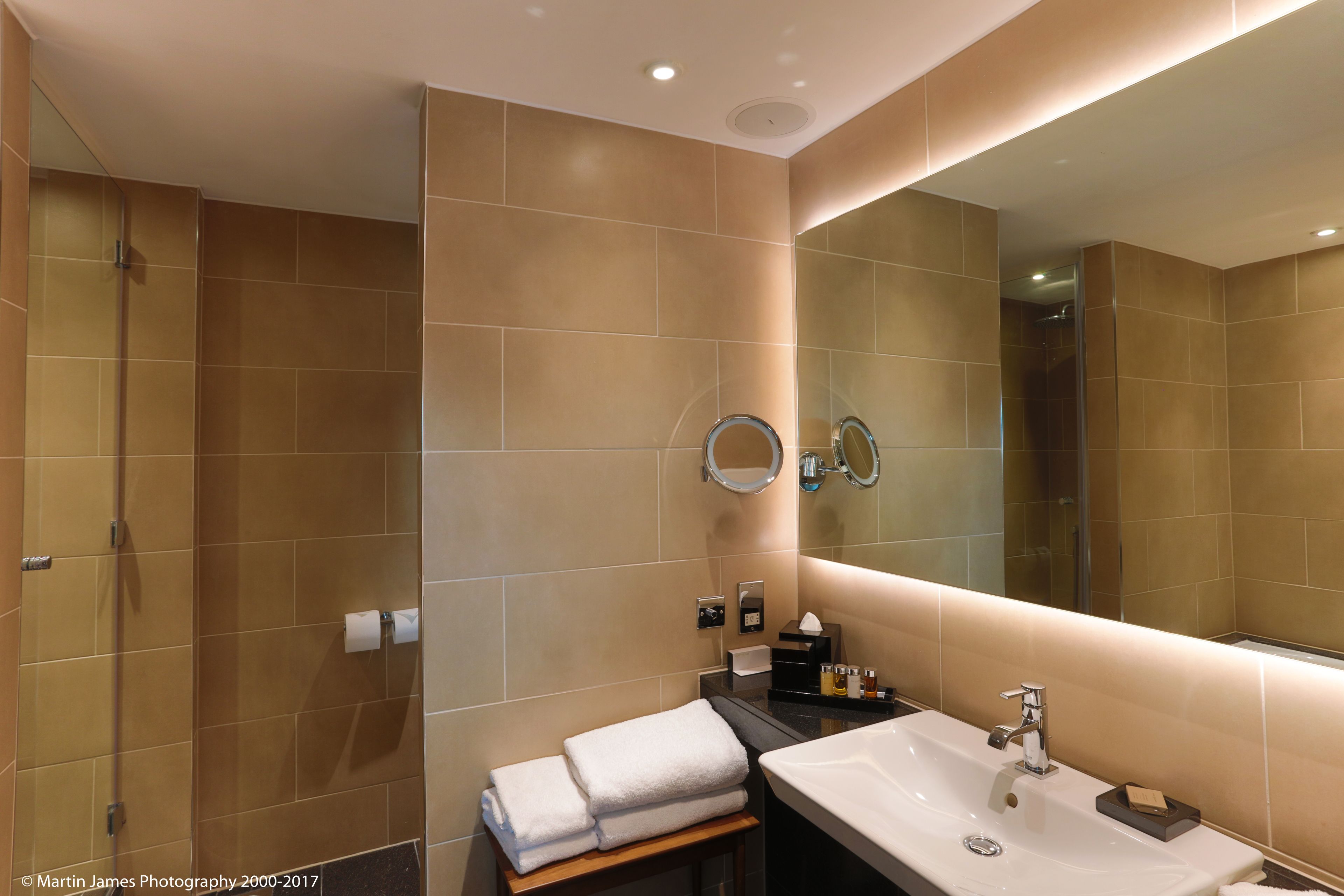 Une salle de bain moderne avec un grand miroir, un lavabo et un espace douche.