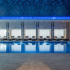 A swimming pool with lounge chairs and patterned wallpaper.