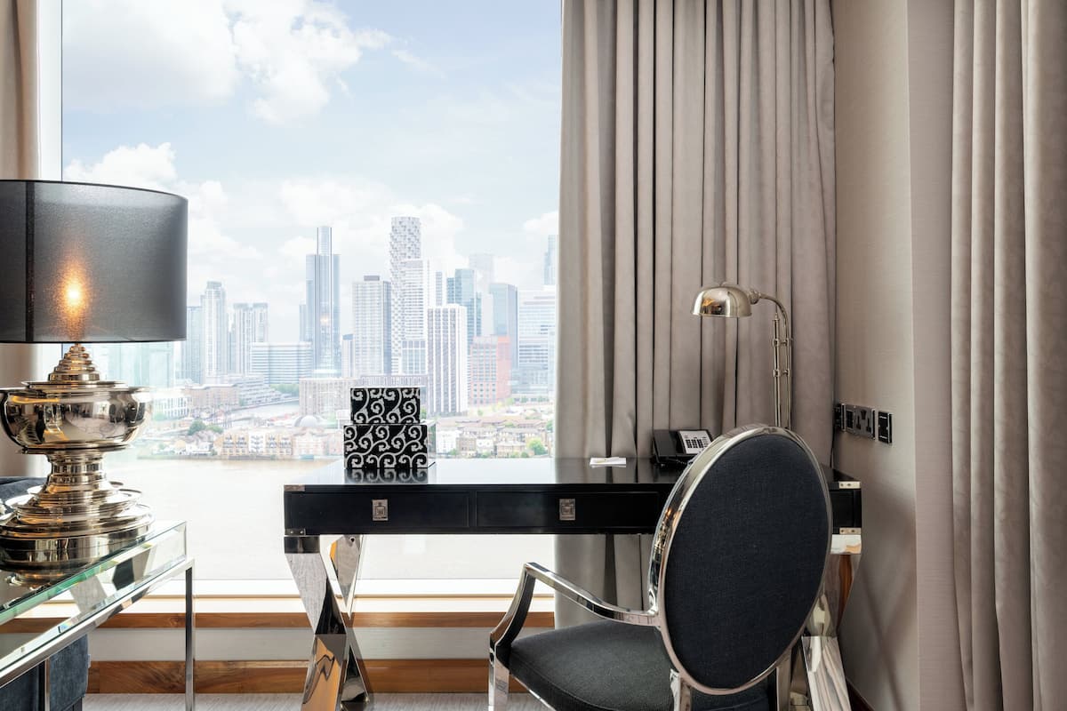 Hotellihuone, jossa on työpöytä, tuoli, lamppu ja näkymä kaupungin siluettiin.