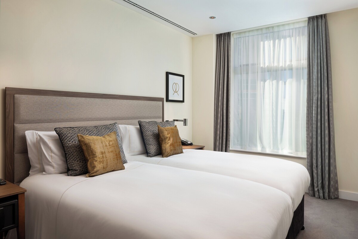 A double bed with a headboard, two bedside tables, a nightstand, and a window with curtains.