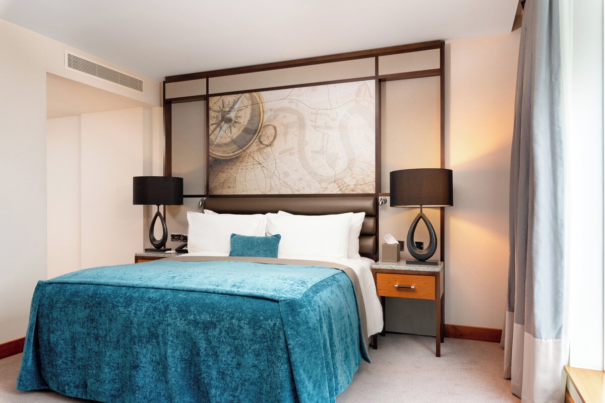 A hotel room with a large bed, two bedside tables with lamps, a large wall map, and a window with curtains.