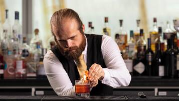 A bartender preparing a drink at a bar with various bottles in the background.
