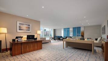 Un amplio vestíbulo de hotel con mostrador de recepción, zona de estar y ventanas grandes que ofrecen vistas a la ciudad.