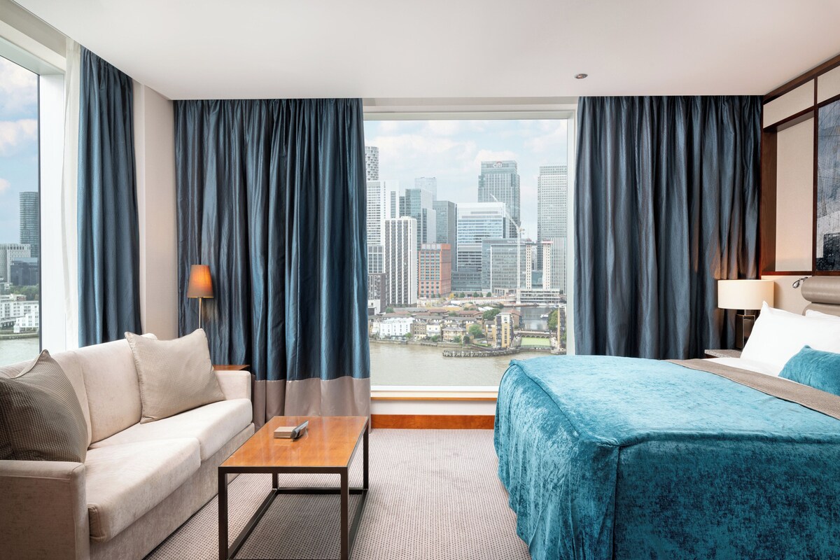 A hotel room with a city view, a sofa, a bed, and a small table.