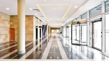 A spacious lobby with a central escalator, glass doors, and a tiled floor.