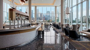 A modern bar area with a city view, featuring a bar counter, seating, and large windows. - InterContinental London - The O2 by IHG (London)