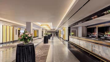 Un vestíbulo de hotel con una larga recepción, mesas negras con jarrones de flores y una lámpara de araña moderna.