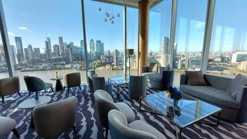 Een moderne lounge met een panoramisch stadsgezicht, met diverse zitplaatsen en een glazen bijzettafeltje.