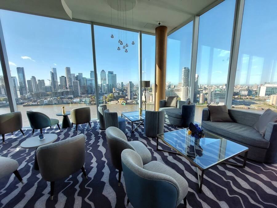 Een moderne lounge met een panoramisch stadsgezicht, met diverse zitplaatsen en een glazen bijzettafeltje.