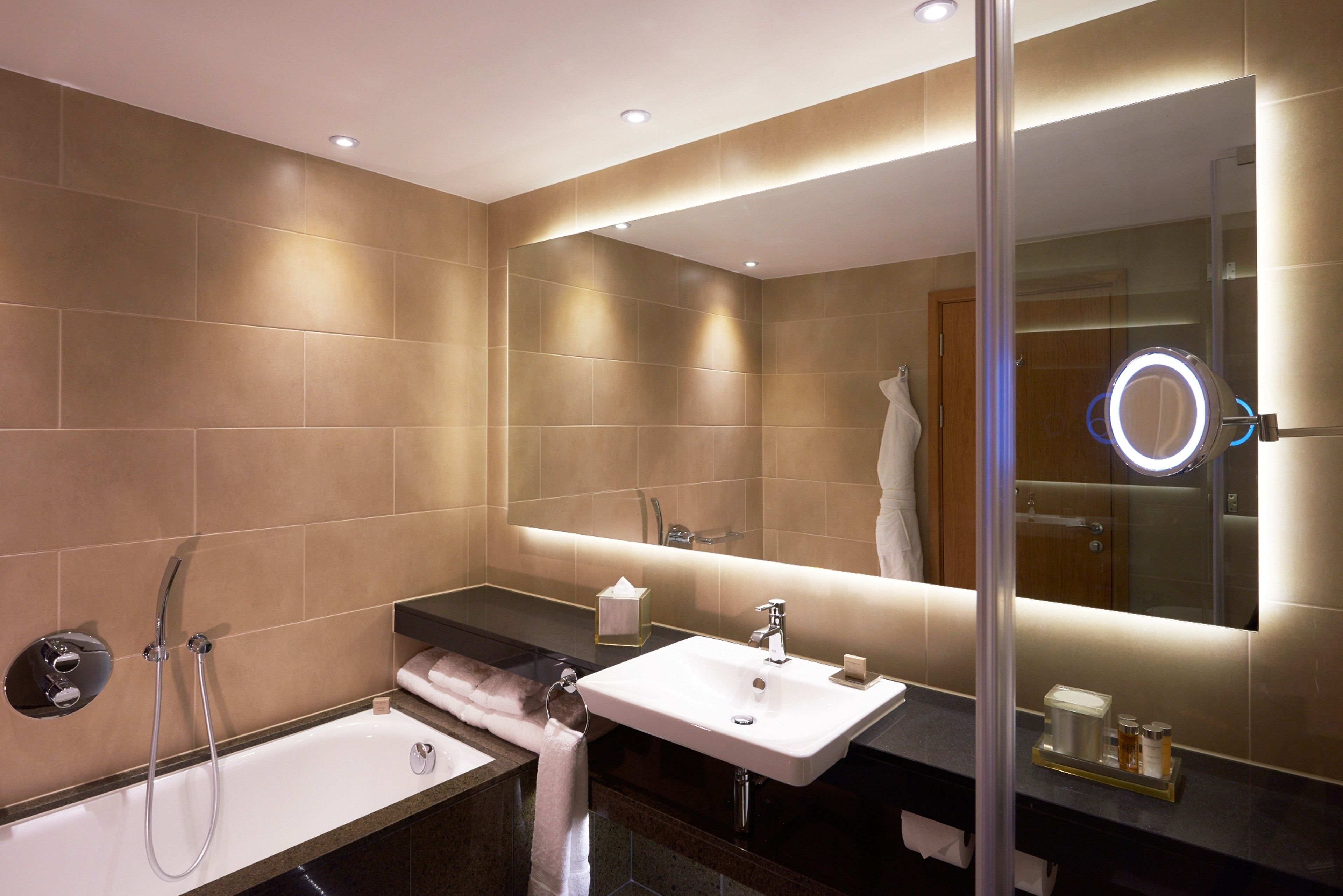 Une salle de bain moderne avec une baignoire, un lavabo et un grand miroir doté d’un anneau lumineux.