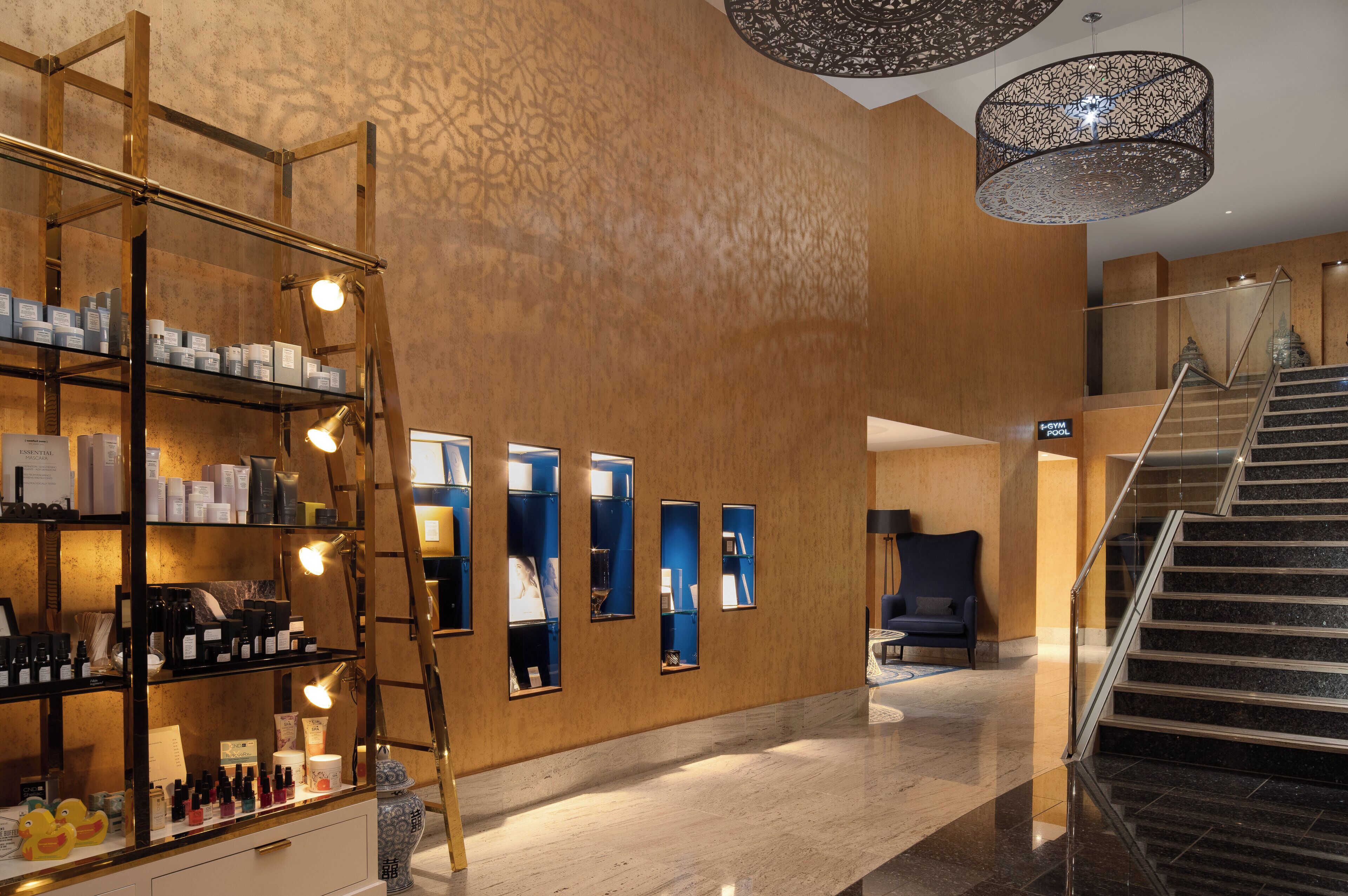 Un hall d’entrée moderne avec un escalier, un comptoir d’accueil et un présentoir de produits de spa.