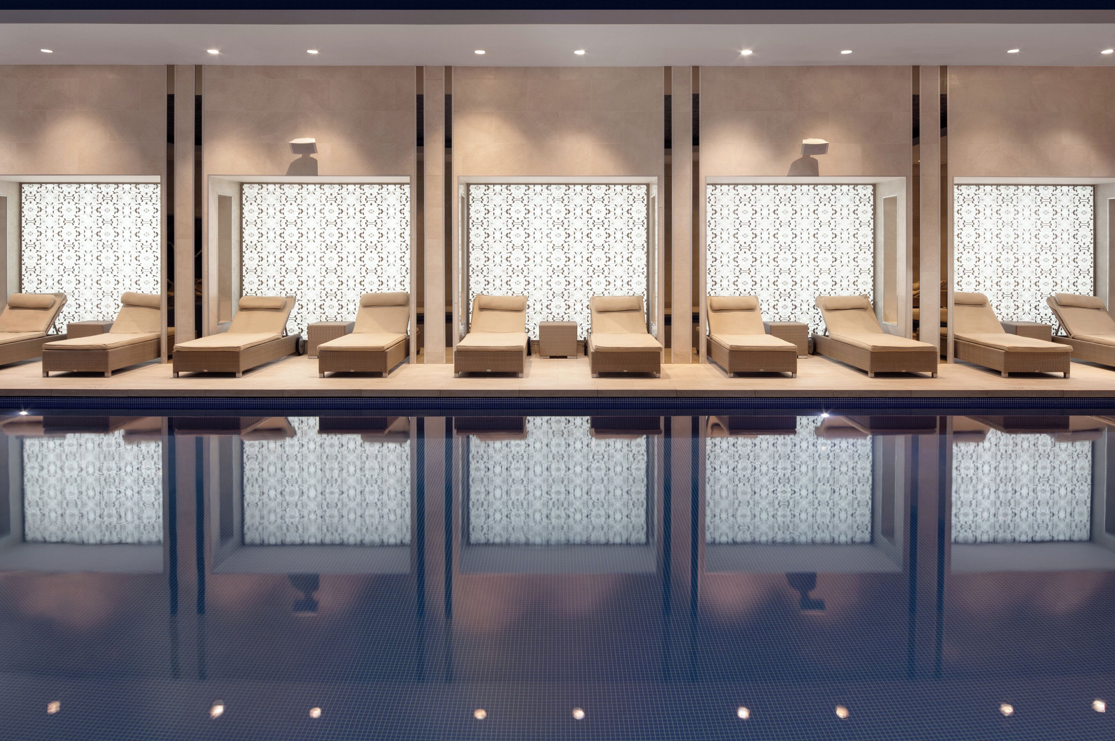 A modern indoor pool area with multiple sun loungers and a patterned wall design.