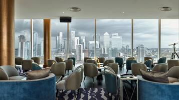 A modern hotel lobby with a panoramic city view, comfortable seating, and a large table.