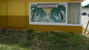 A building with a yellow exterior and a mural of a parrot and palm trees.