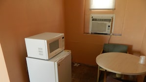 A compact kitchenette with a microwave on top of a refrigerator, a small table, and a chair.