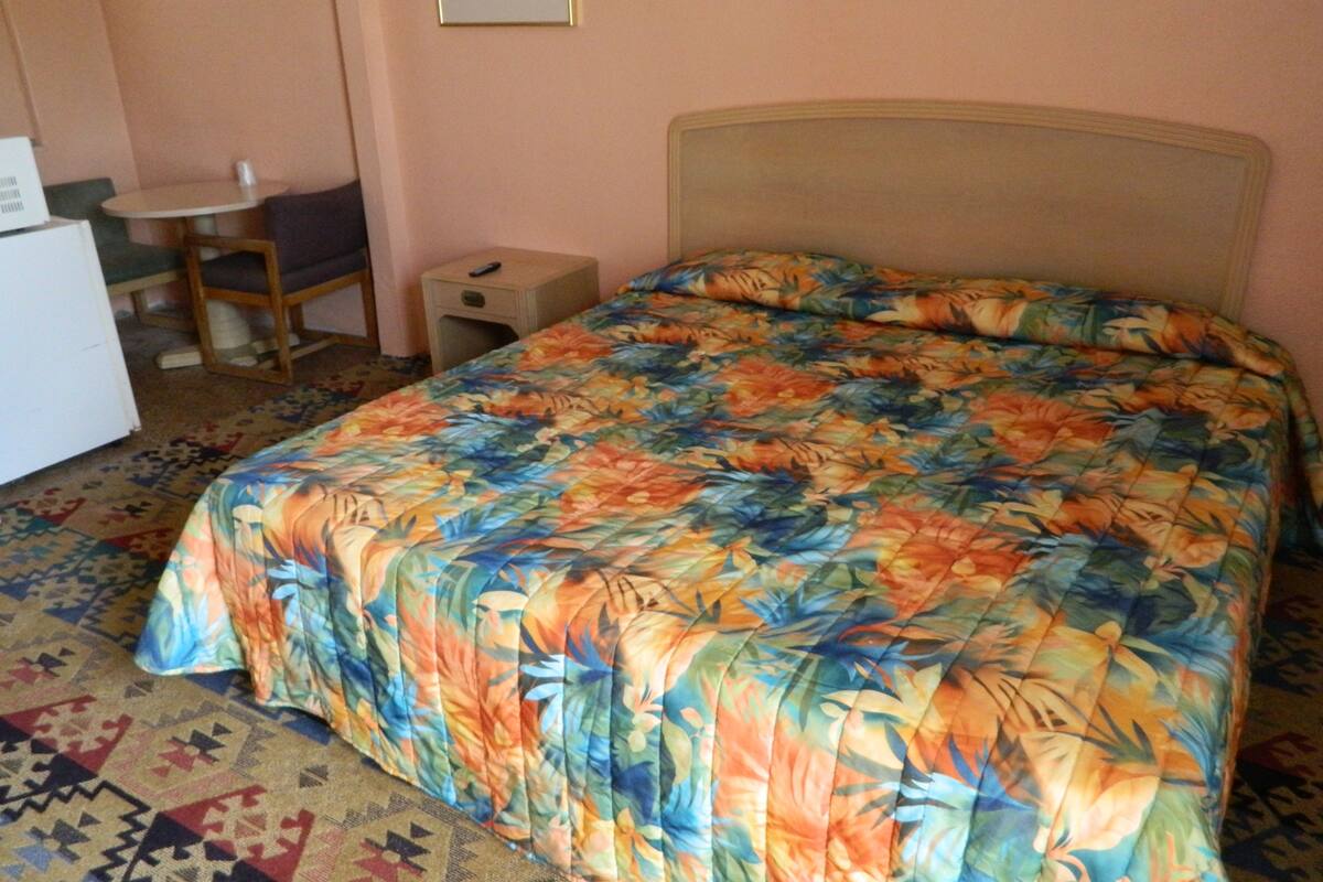 A room with a bed, a small table, a chair, and a nightstand.