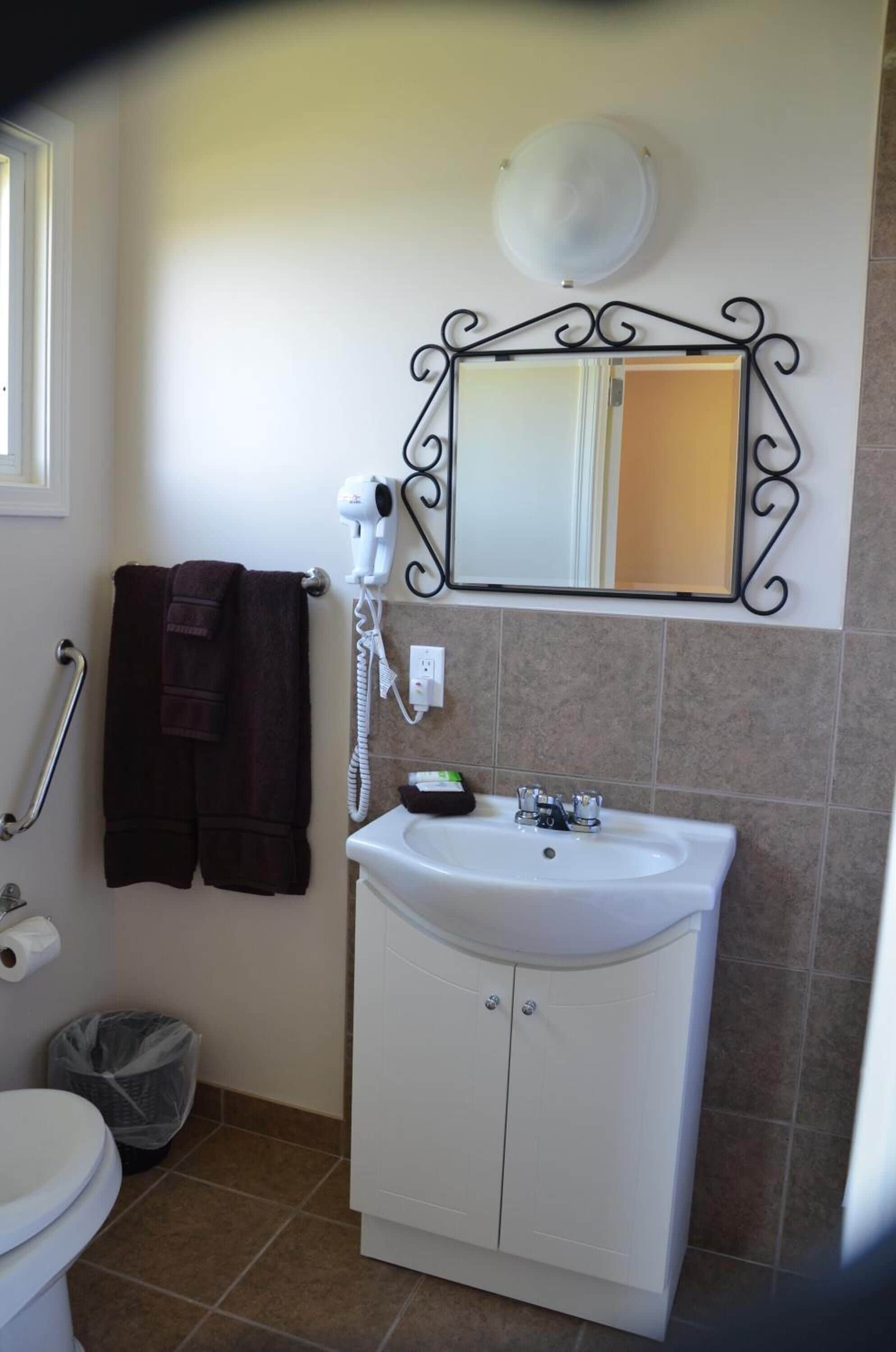 A bathroom with a white sink, a mirror with a decorative frame, a hairdryer, and a towel rack.