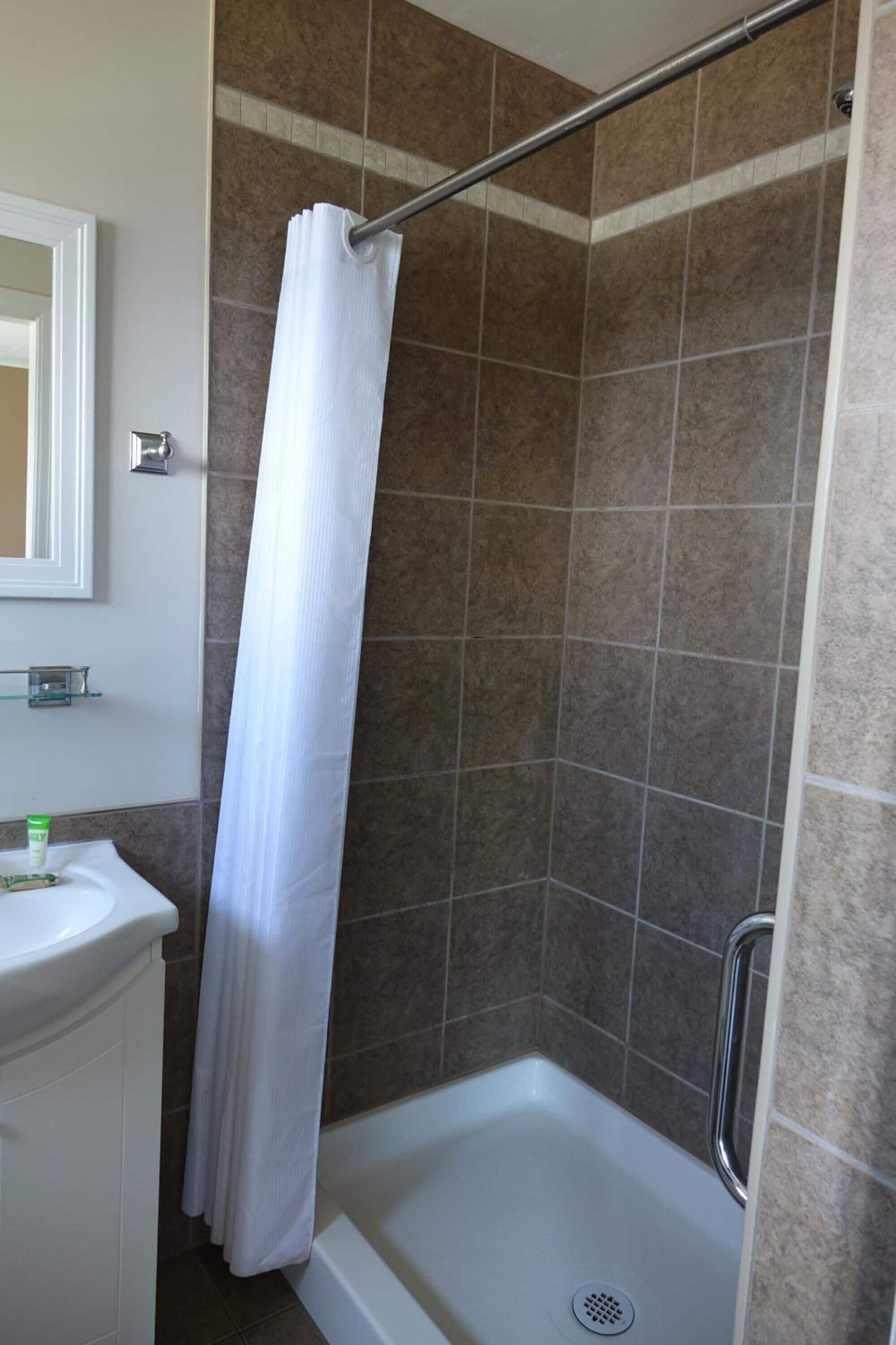A shower area with a white curtain, a glass shelf with toiletries, and a white sink.
