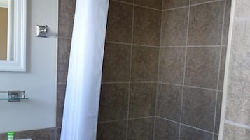 A shower area with a white curtain, a glass shelf with toiletries, and a white sink.
