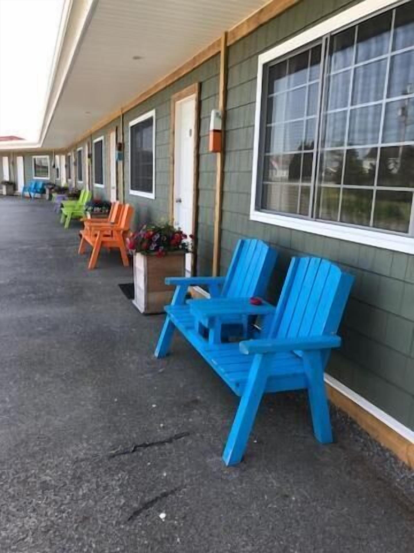 A row of single-story buildings with large windows and a covered outdoor area with colorful Adirondack chairs.