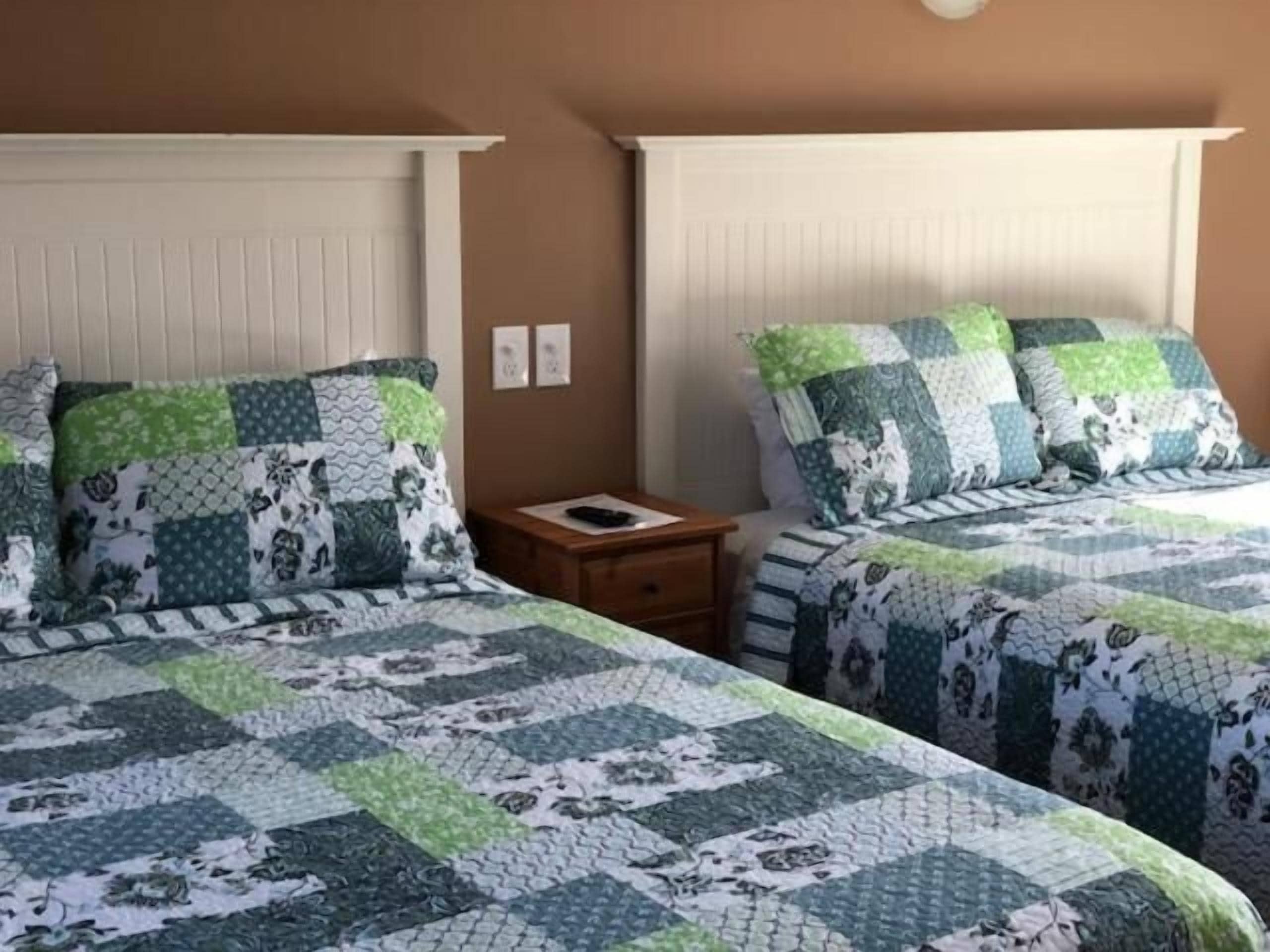 Una habitación con dos camas, cada una con colcha acolchada y almohadas a juego. Entre las camas hay una mesita de noche de madera con un control remoto encima.
