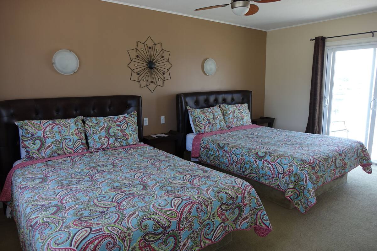 A bedroom with two beds, a ceiling fan, a decorative wall piece, and a window with curtains.