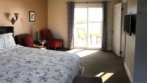 Un dormitorio con una cama grande, un ventilador de techo, un televisor y vistas al exterior a través de una puerta corrediza.