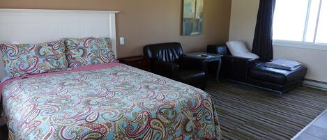 A hotel room with a large bed, a desk, a chair, and a sofa.