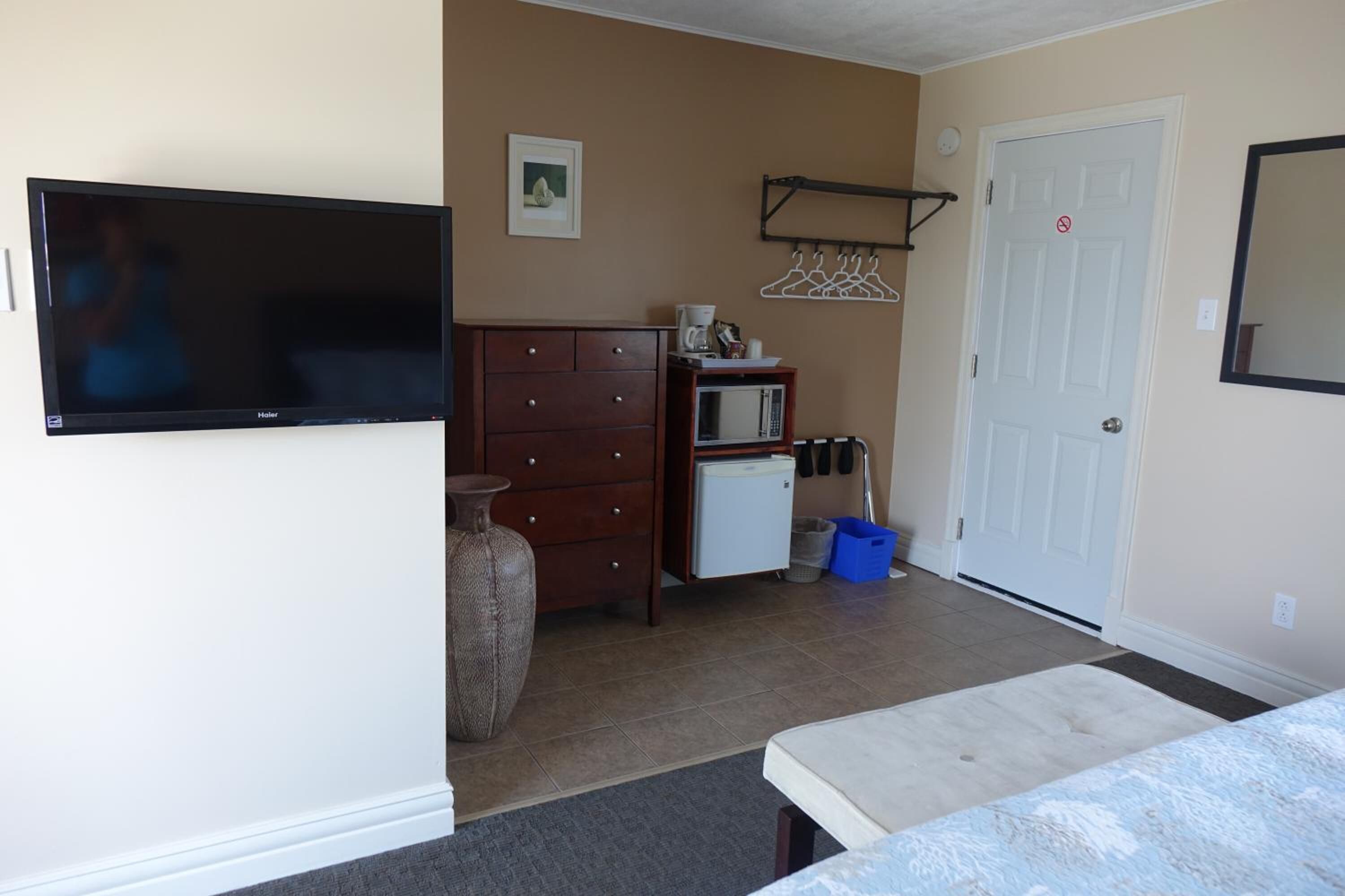 Una habitación con televisión de pantalla plana, cómoda de madera, microondas, refrigerador pequeño, puerta con perchero y aro de baloncesto.
