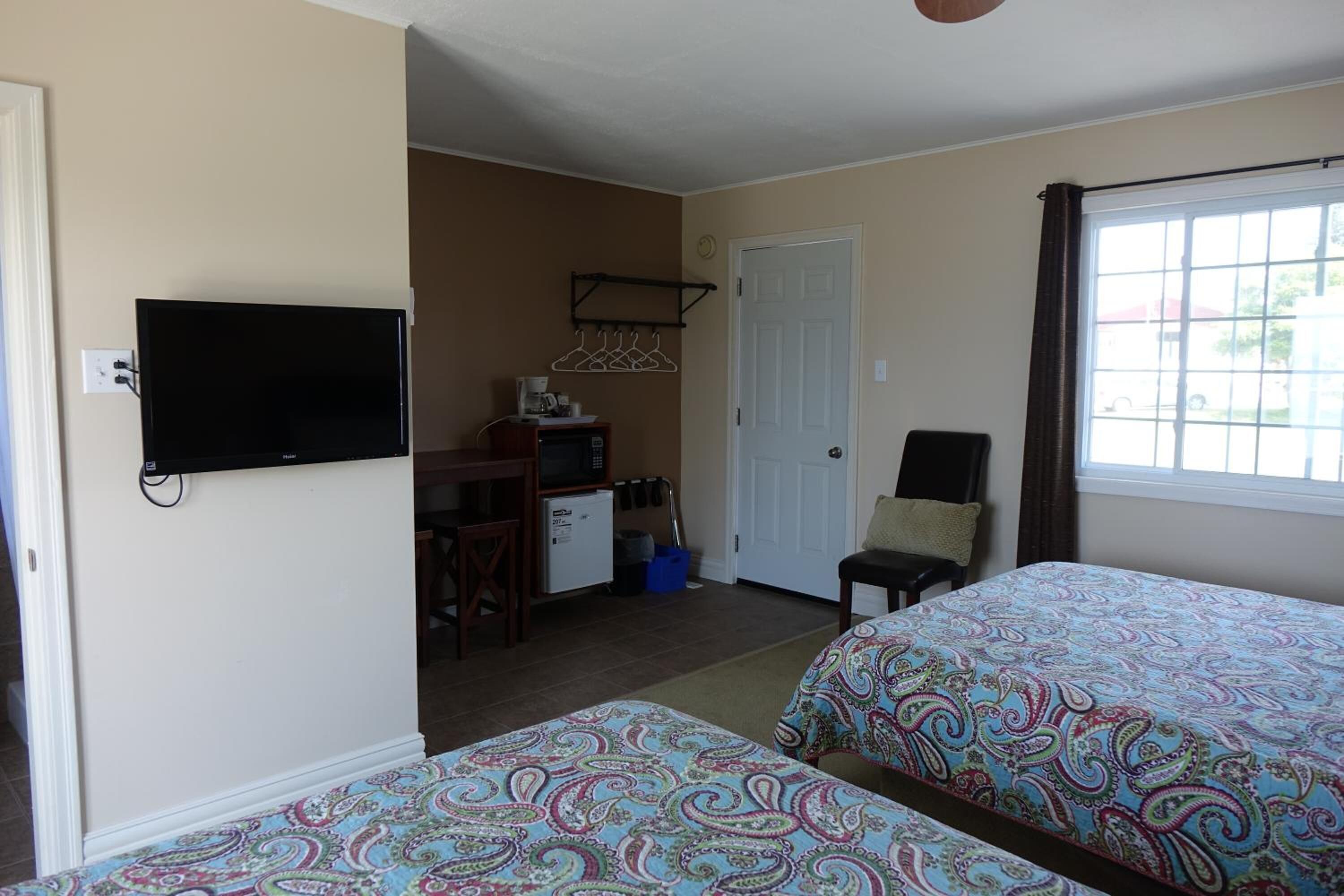 A hotel room with two beds, a TV, a desk with a computer, a chair, and a window with curtains.