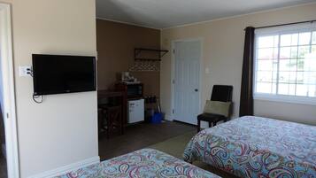 A hotel room with two beds, a TV, a desk with a computer, a chair, and a window with curtains.