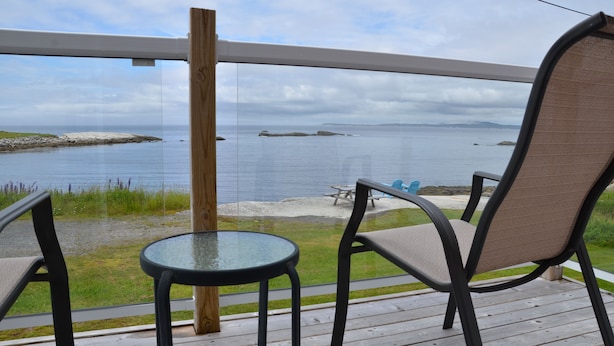 Terraza con mesa de vidrio y dos sillas con vista a una costa rocosa y mar tranquilo.