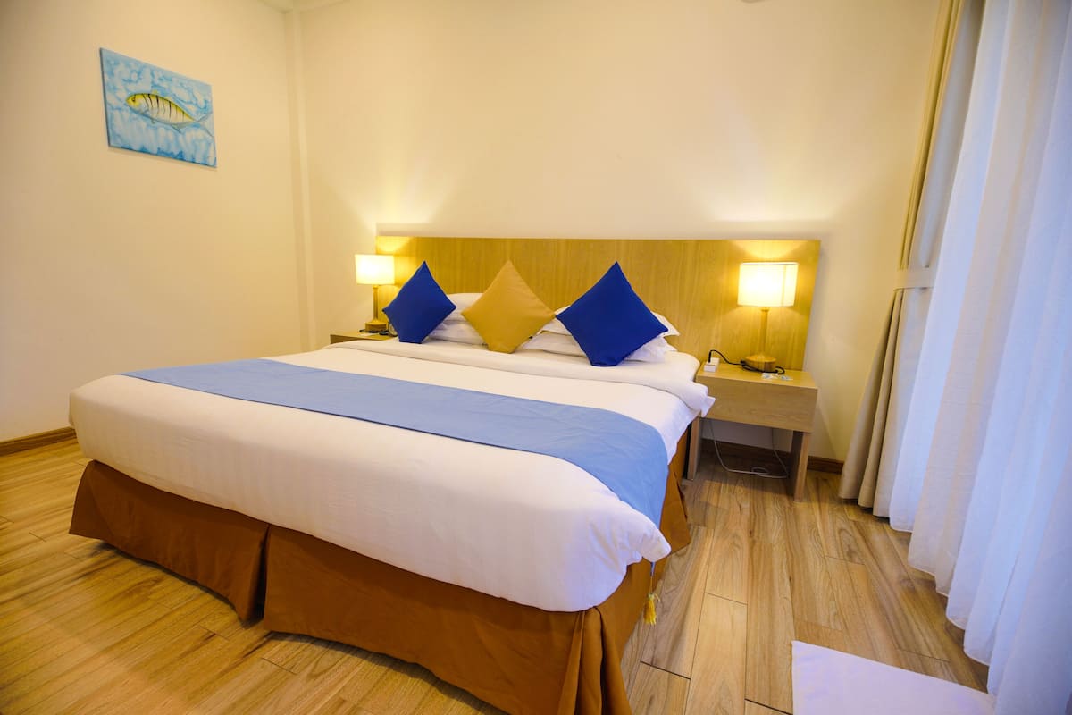 Une chambre d’hôtel avec un grand lit, deux tables de chevet avec des lampes, une tête de lit en bois et un tableau au mur.