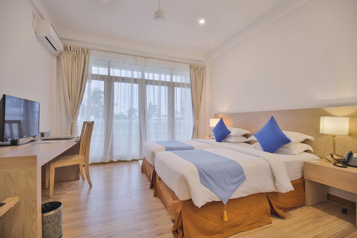 Une chambre d’hôtel avec deux lits, un bureau, une chaise, une télévision et une lampe.