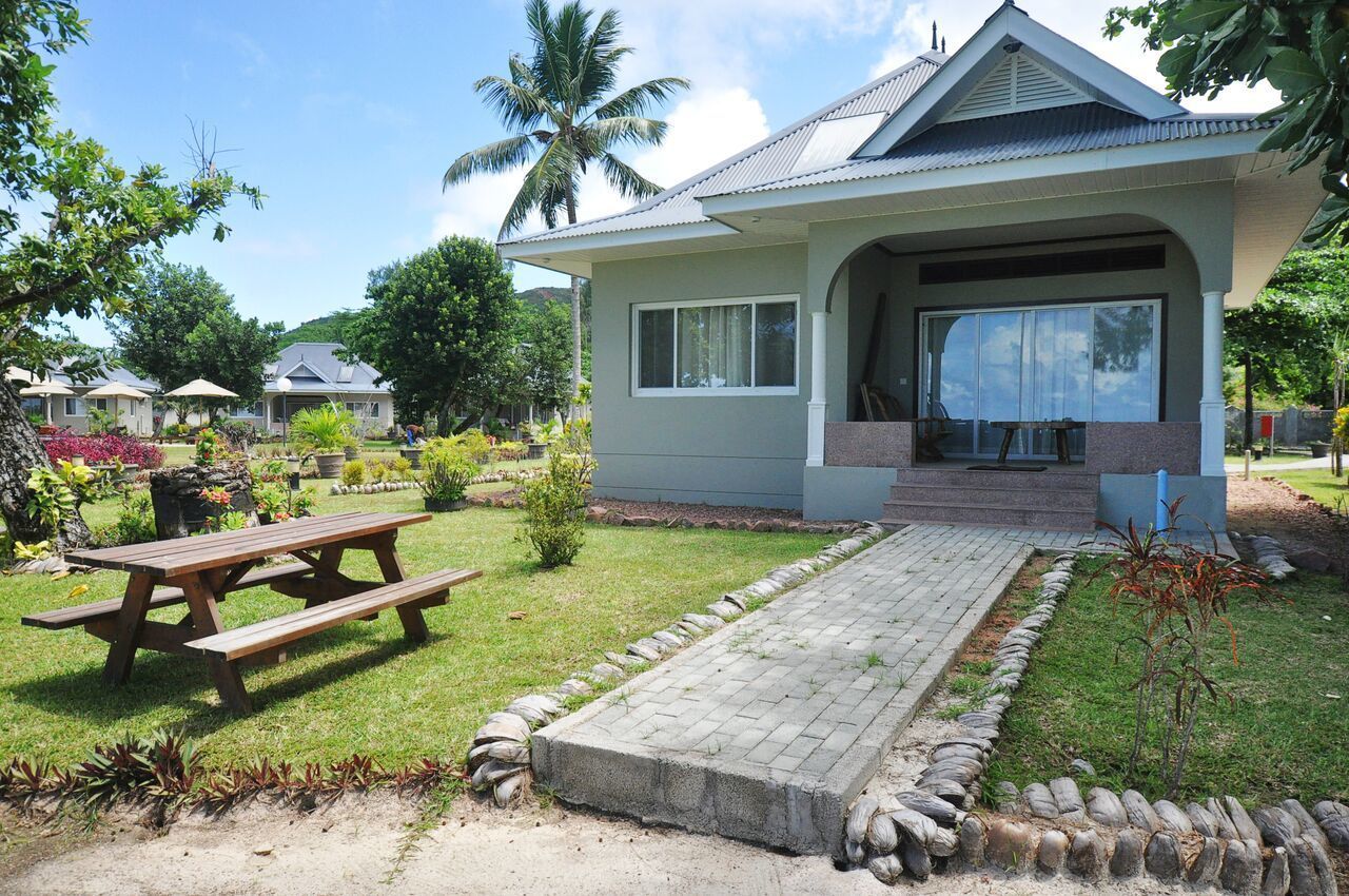 A single-story house with a covered porch, a paved driveway, and a garden with various plants and a picnic table.