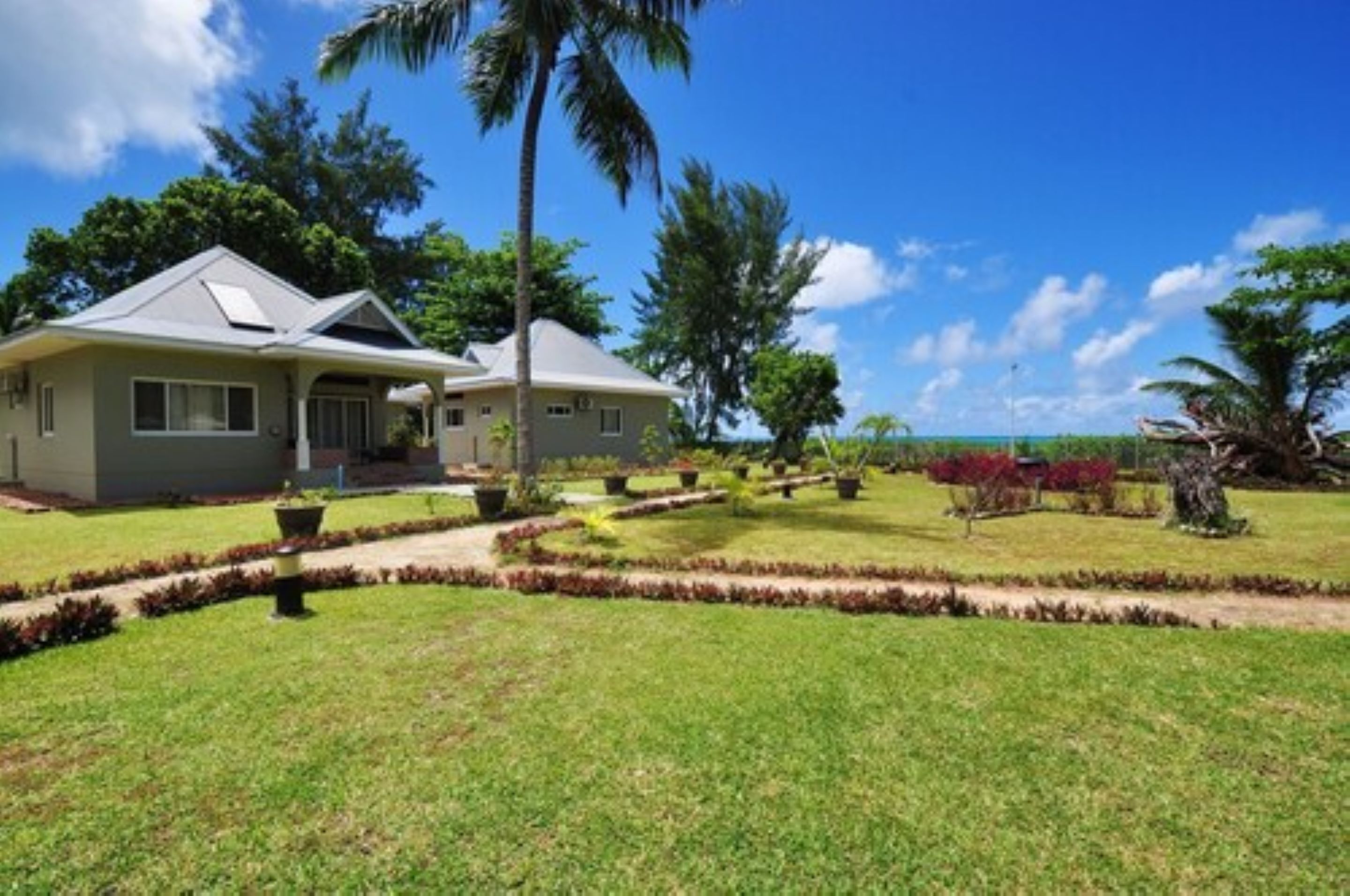 A two-story house with a well-maintained lawn, palm trees, and a clear view of the ocean.