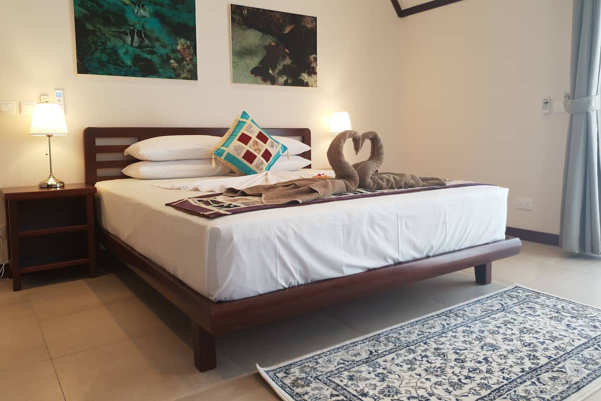 A hotel room with a bed, two wall-mounted paintings, a nightstand with a lamp, and a decorative swan towel.