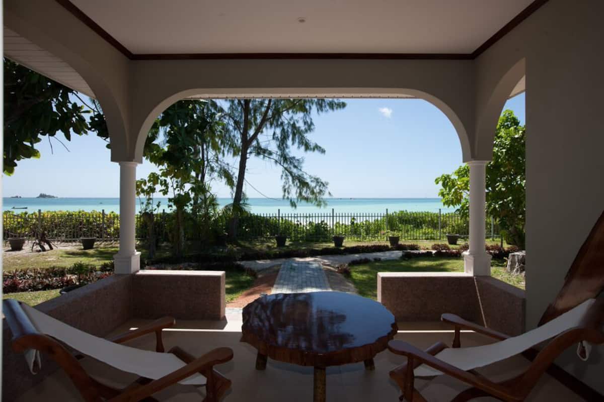 A covered outdoor seating area with a view of the sea and a vineyard.
