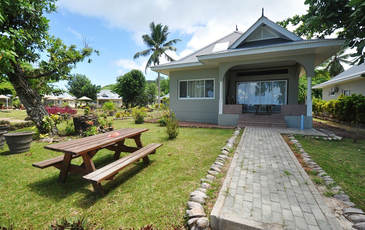 A house with a covered patio, a wooden picnic table, and a paved pathway.