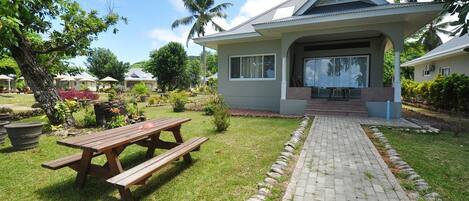 A house with a covered patio, a wooden picnic table, and a paved pathway.