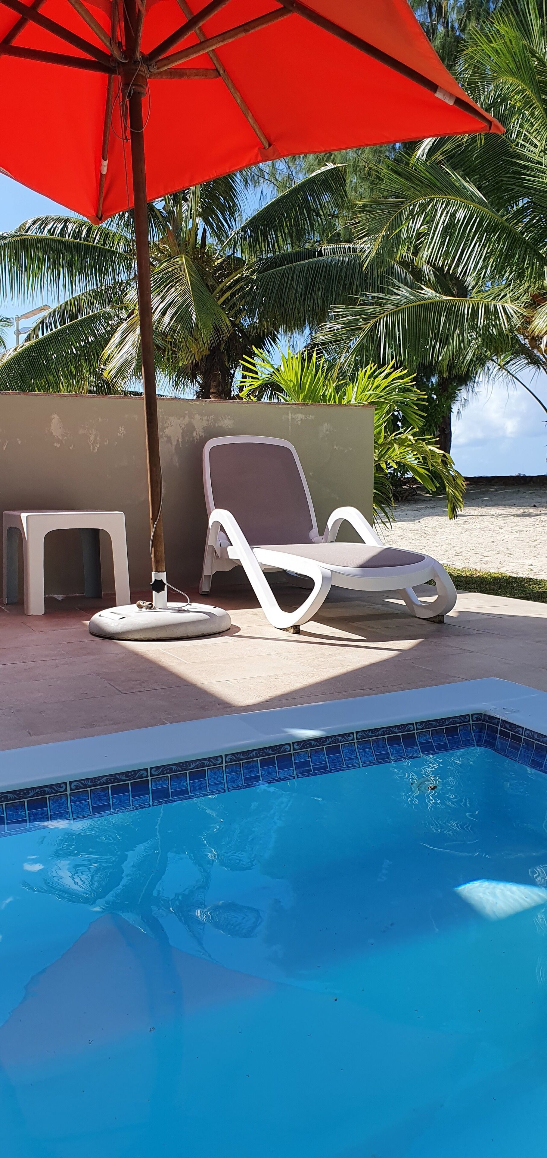 Ein Pool mit zwei weißen Liegestühlen und einem roten Sonnenschirm.