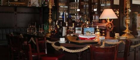 Una zona de bar con sillas de madera, barra y diversos botellas y vasos.