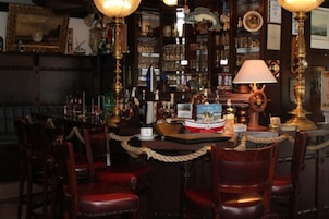 Una zona de bar con sillas de madera, barra y diversos botellas y vasos.