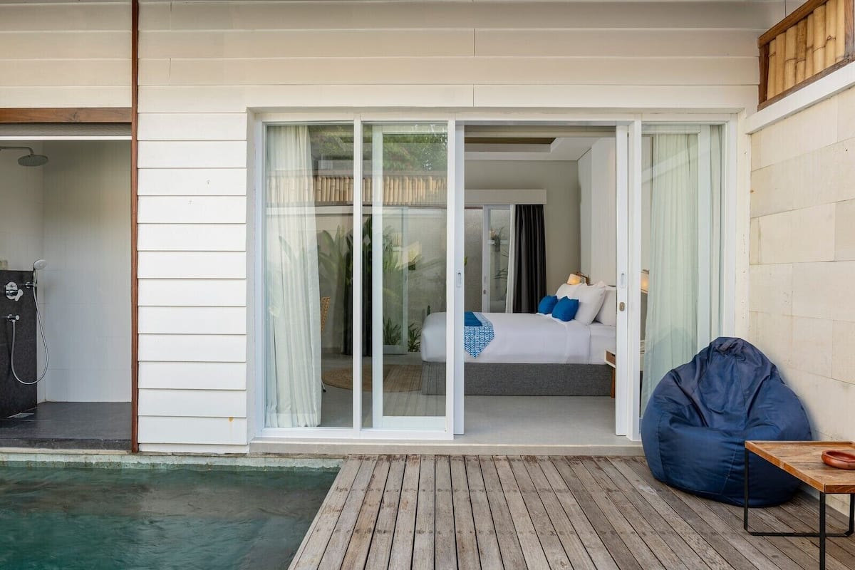 Une chambre avec un lit, un pouf bleu et une petite table.