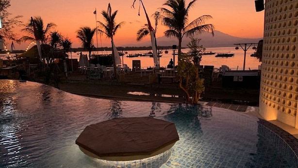 Ein unendlicher Pool mit Whirlpool, Palmen und Blick auf den Sonnenuntergang.
