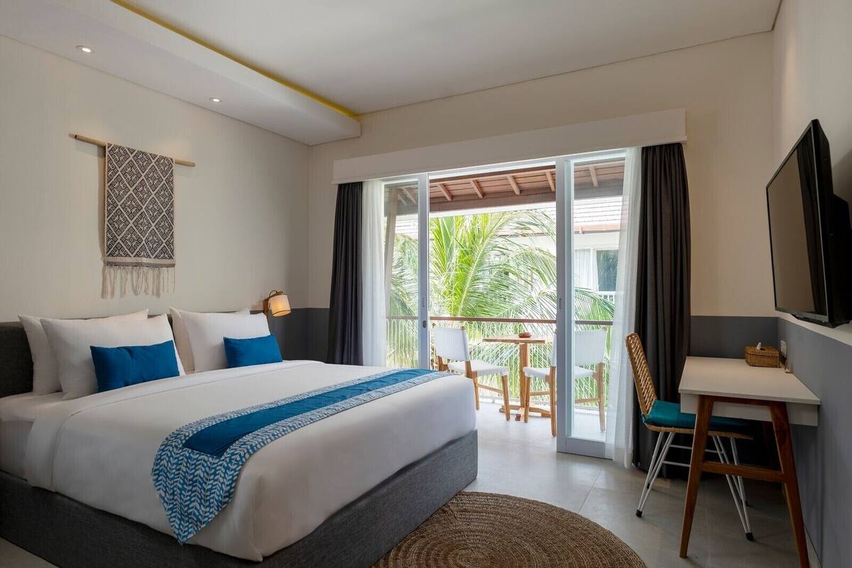 Une chambre d’hôtel avec un grand lit, un bureau, une chaise, une télévision et un balcon offrant une vue sur les palmiers.