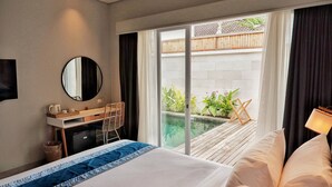 Ein Hotelzimmer mit Bett, Schreibtisch, Stuhl, Spiegel und Blick auf einen Garten durch eine Schiebetür.