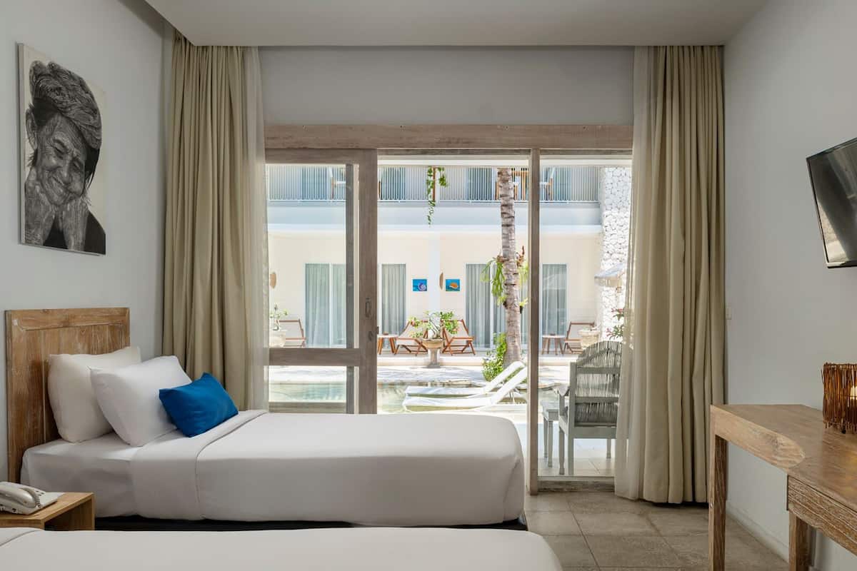 Une chambre d’hôtel équipée d’un lit, d’un bureau et offrant une vue sur l’espace extérieur, qui comprend une piscine et des chaises longues.