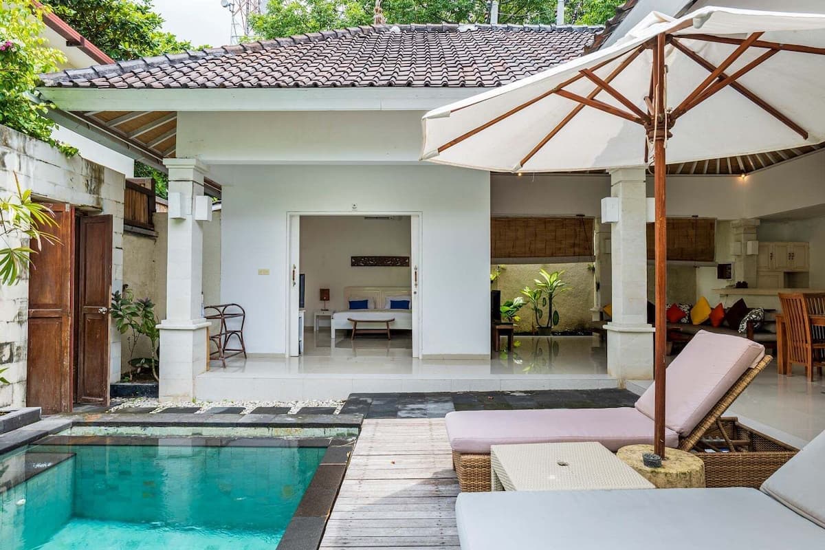 Un espace aménagé au bord de la piscine, avec une terrasse en bois, une chaise longue et un coin salon couvert, agrémenté d’un parasol.