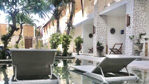Ein Poolbereich mit Korlounge-Stühlen, einer Steinmauer und tropischen Pflanzen.